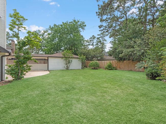 Spacious backyard with lush grass, mature trees, and a wooden fence for privacy. Ideal for outdoor activities and relaxation. | Image 38