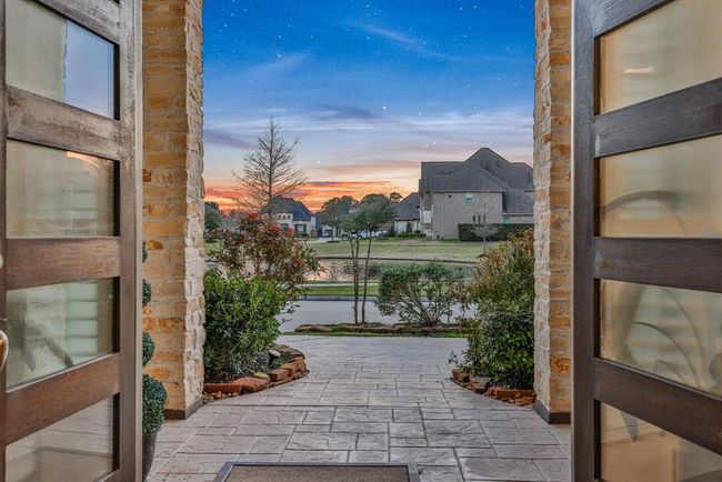 The welcoming front entrance with elegant double doors, leading to a paved walkway surrounded by lush greenery. The view opens up to no front neighbors. | Image 9