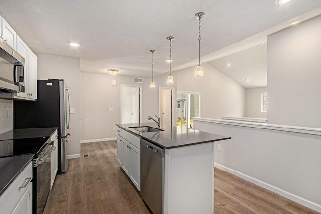 Bright, white kitchen cabinetry is accented by white quartz counters and tile backsplash. The kitchen island provides prep and sitting space and is accented by pendant lighting above. Stainless steel appliances are included! | Image 6