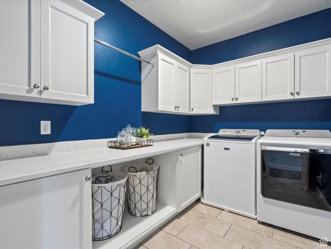 Clothes washing area with cabinet space, washing machine and dryer, light tile patterned flooring, and a textured ceiling | Image 29
