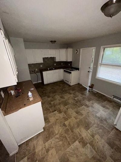 Kitchen featuring decorative backsplash, baseboard heating, stove, and white cabinets | Image 3