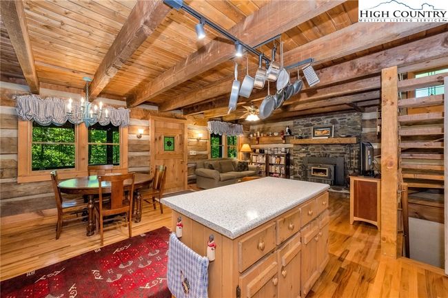 The kitchen, dining, and living areas blend effortlessly beneath rustic beamed ceilings, and the native stone fireplace anchors the room with elemental character. | Image 7