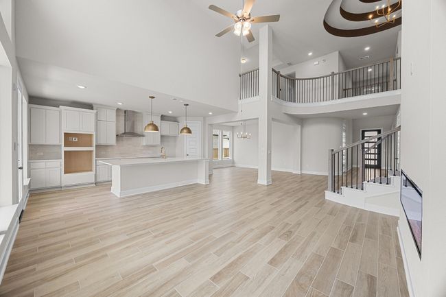 Unfurnished living room with a towering ceiling, a chandelier, stairway, light wood-style floors, and recessed lighting | Image 8