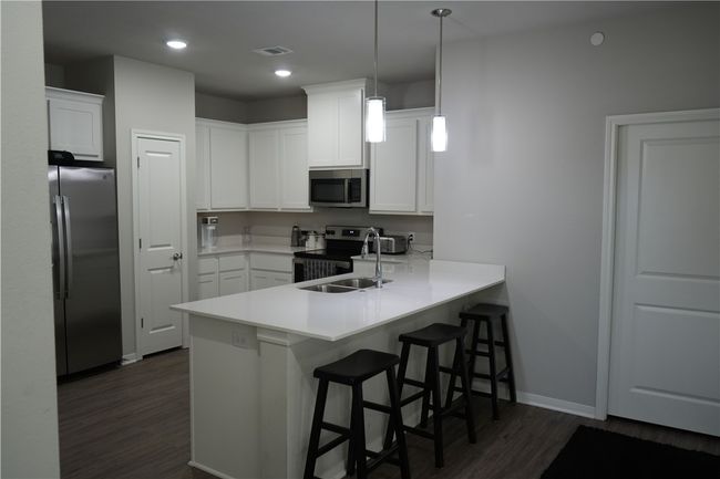 Kitchen with appliances with stainless steel finishes, dark wood-style flooring, a peninsula, a kitchen breakfast bar, and light countertops | Image 4