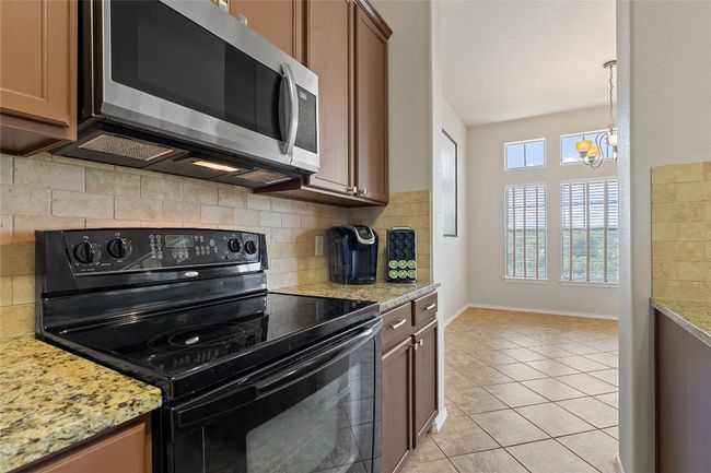 Kitchen with stainless steel microwave, a chandelier, light tile patterned floors, black electric range, and decorative backsplash | Image 29