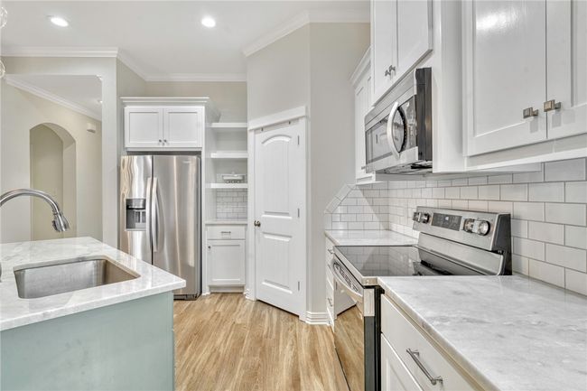 Kitchen with appliances with stainless steel finishes, light wood-type flooring, white cabinetry, decorative backsplash, and crown​​‌​​​​‌​​‌‌​‌‌​​​‌‌​​‌‌​‌​​​​​‌ molding | Image 9