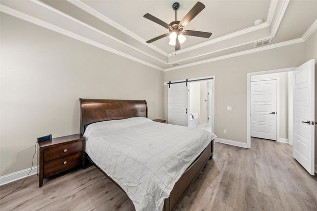 Bedroom with light wood-style floors, crown molding, a tray ceiling, visible vents, and baseboards | Image 10
