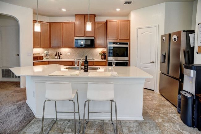 Kitchen featuring stainless steel appliances, light countertops, decorative backsplash, hanging light fixtures, and recessed lighting | Image 4