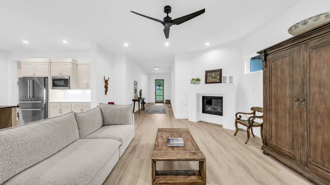 Living area featuring recessed lighting, light wood-type flooring, ceiling fan, a glass covered fireplace, and baseboards | Image 14