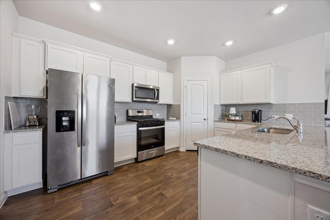 Kitchen with appliances with stainless steel finishes, white cabinetry, dark wood-style floors, light stone counters, and recessed lighting | Image 18