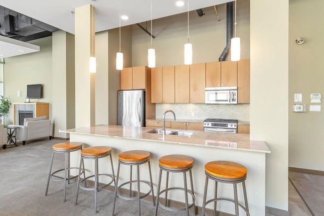 Kitchen featuring appliances with stainless steel finishes, light stone counters, a breakfast bar, backsplash, and hanging light fixtures | Image 26