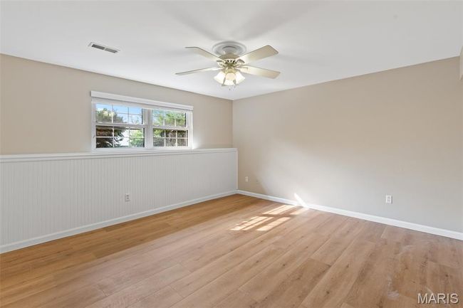 Empty room with a ceiling fan, a wainscoted wall, light wood-style floors, and baseboards | Image 24
