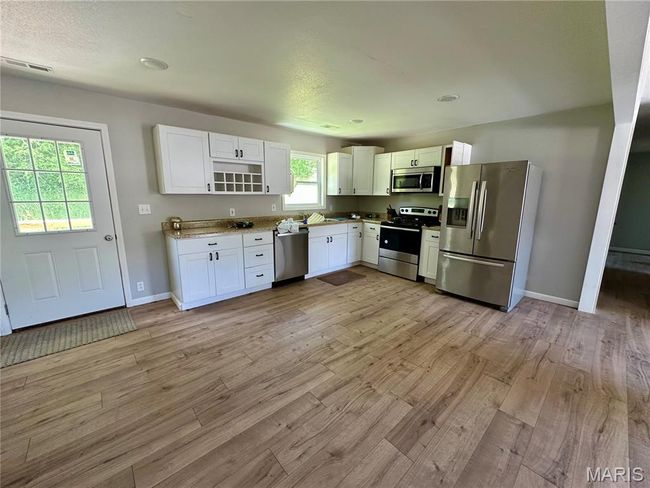 Kitchen with stainless steel appliances, light wood-type flooring, white cabinetry, open shelves, and light countertops | Image 6