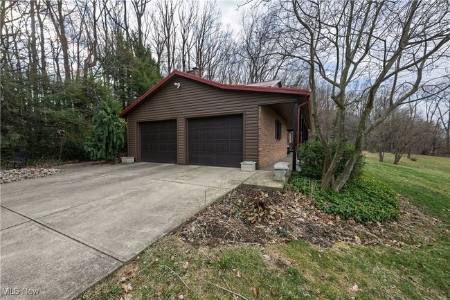 View of home's exterior featuring a chimney, concrete driveway, an attached garage, brick siding, and a lawn | Image 9