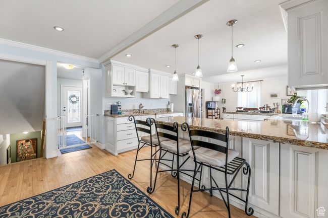 Kitchen featuring light stone counters, a peninsula, crown molding, white cabinetry, and stainless steel refrigerator with ice dispenser | Image 14
