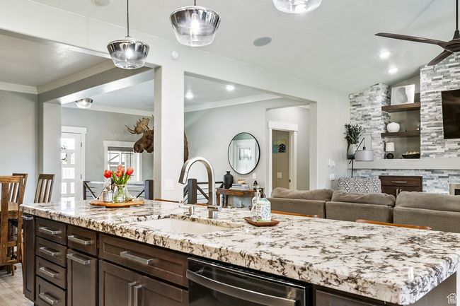 Kitchen featuring black dishwasher, a ceiling fan, light stone counters, open floor plan, and ornamental molding | Image 27