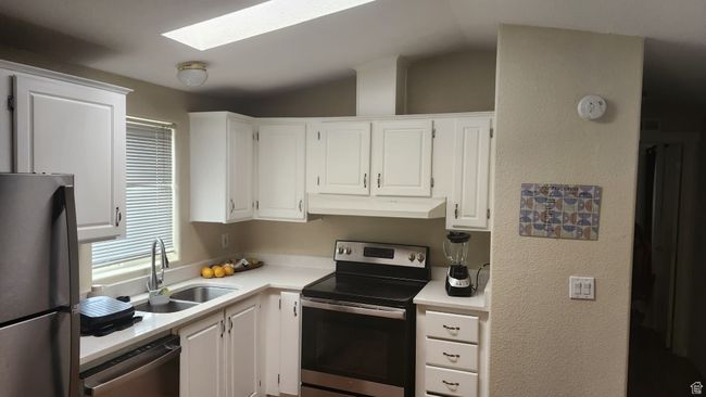 Kitchen with appliances with stainless steel finishes, under cabinet range hood, a sink, light countertops, and white cabinets | Image 9