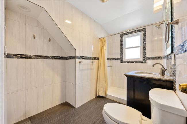Bathroom featuring tile walls, tiled shower, vanity, toilet, and lofted ceiling | Image 13