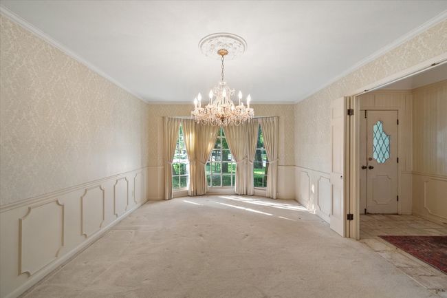 Wool carpeted dining room with crystal chandelier, wallpapered walls, wainscoting, and gorgeous wood bay window | Image 4