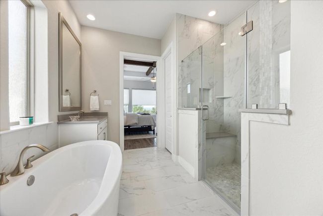The freestanding tub and extended walk-in shower with two shower heads (including a rain head) offer multiple options to unwind, while the shower also features a convenient seated bench for added comfort. | Image 21