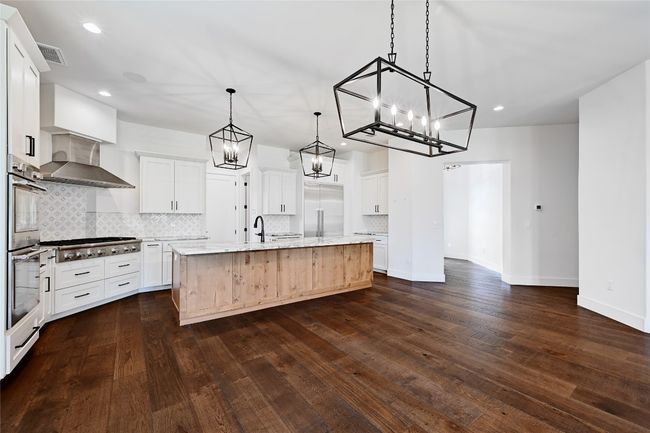 Kitchen featuring dark wood-style flooring, appliances with stainless steel finishes, wall chimney range hood, and a kitchen island with sink | Image 8