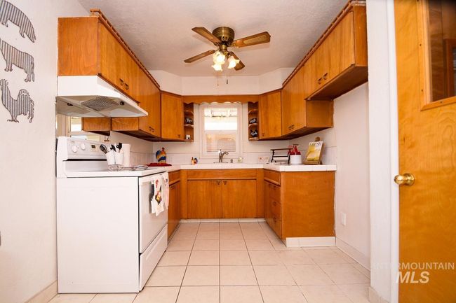 Kitchen featuring white electric stove, under cabinet range hood, a ceiling fan, brown cabinetry, and light countertops | Image 11
