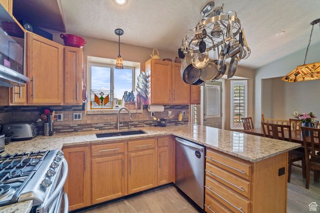 Kitchen featuring a textured ceiling, decorative backsplash, a sink, appliances with stainless steel finishes, and a peninsula | Image 9
