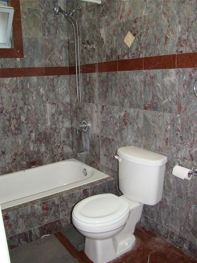 Bathroom featuring tiled shower / bath combo, tile patterned flooring, tile walls, and toilet | Image 12
