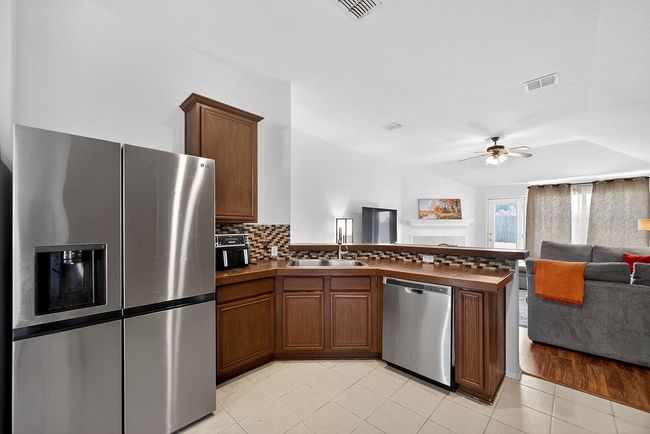 Kitchen with stainless steel appliances, open floor plan, dark countertops, ceiling fan, and a peninsula | Image 7