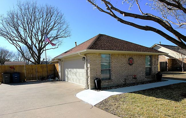 View of property exterior featuring brick siding, roof with shingles, concrete driveway, and fence | Image 8