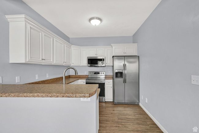Kitchen with appliances with stainless steel finishes, a peninsula, dark wood-type flooring, and white cabinets | Image 8