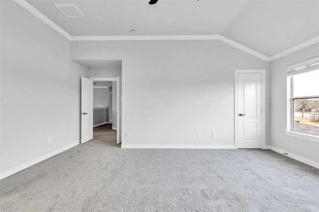This photo shows a spacious, bright room with neutral gray walls and carpet, featuring a high ceiling and white trim. It includes a window for natural light, two doors, and clean lines, offering a blank canvas for personalization. | Image 27