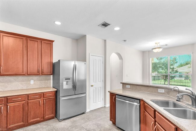 Kitchen featuring appliances with stainless steel finishes, decorative backsplash, brown cabinetry, recessed lighting, and light tile patterned floors | Image 8