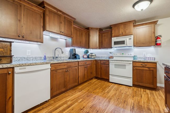Kitchen with a textured ceiling, light wood-style floors, white appliances, and a sink | Image 46