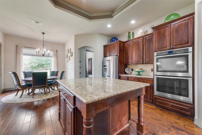 Kitchen featuring stainless steel appliances, a tray ceiling, dark wood-style floors, arched walkways, and light stone counters | Image 19