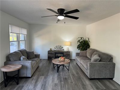 Living room featuring dark wood-type flooring, a fireplace, a textured ceiling, and ceiling fan | Image 2