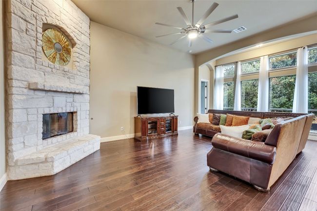Living room featuring a limestone fireplace, a ceiling fan, dark wood-type flooring, and arched walkways | Image 18
