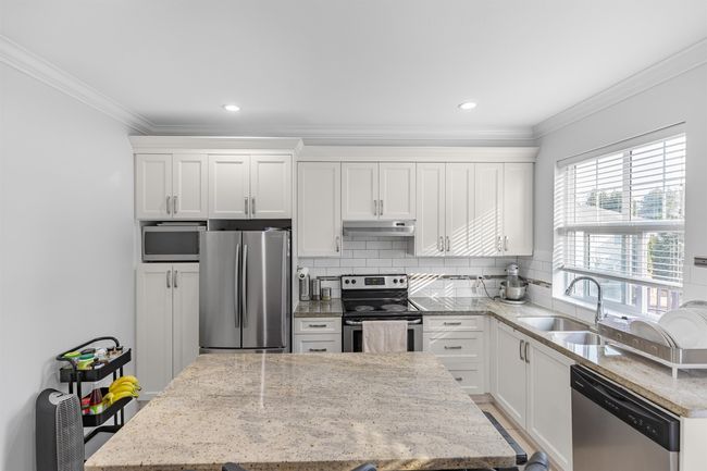 Kitchen featuring appliances with stainless steel finishes, under cabinet range hood, crown molding, a kitchen island, and white cabinetry | Image 7