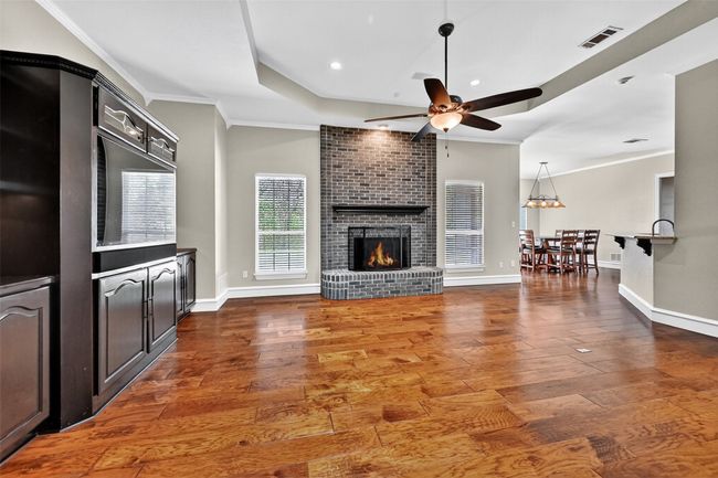 Living room with ceiling fan, wood finished floors, a tray ceiling, a brick fireplace, and ornamental molding | Image 12