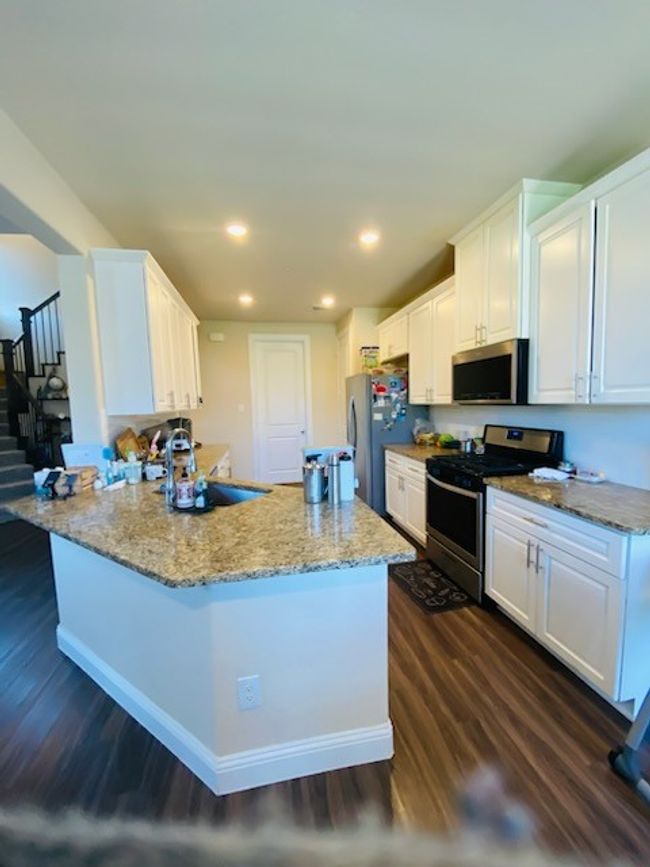 Kitchen featuring appliances with stainless steel finishes, dark wood finished floors, white cabinets, light stone counters, and a peninsula | Image 16
