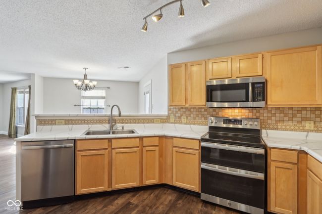 kitchen with stainless steel appliances, a sink, a peninsula, a chandelier, and dark wood-style floors | Image 28