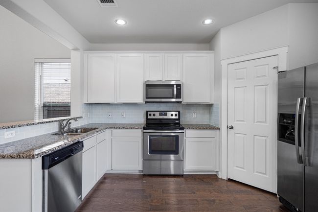 Kitchen with appliances with stainless steel finishes, stone counters, white cabinets, decorative backsplash, and dark wood-style floors | Image 17