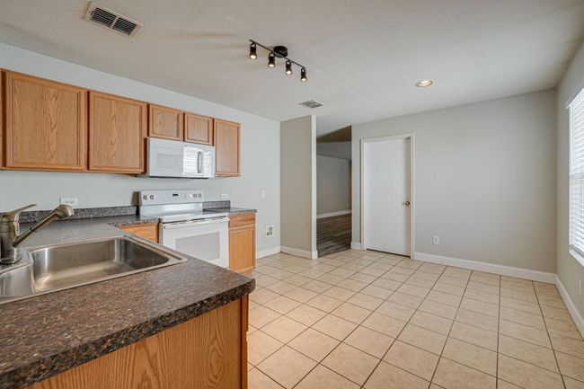 Kitchen with white appliances, dark countertops, light tile patterned floors, recessed lighting, and track lighting | Image 9