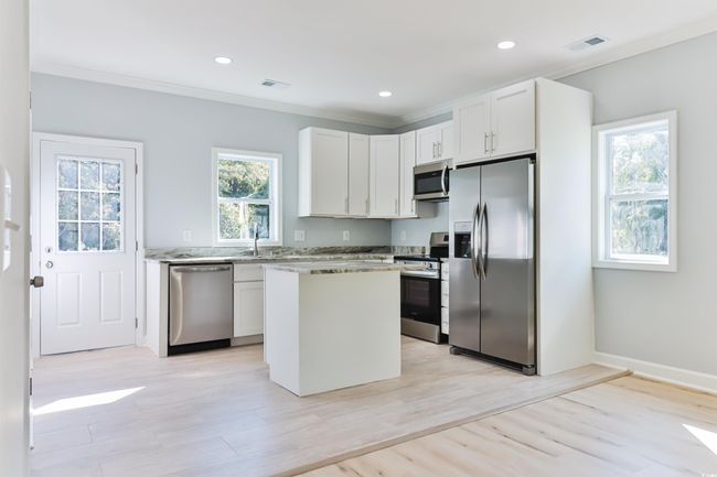 Kitchen featuring light hardwood / wood-style floors, appliances with stainless steel finishes, a kitchen island, and white cabinetry | Image 9