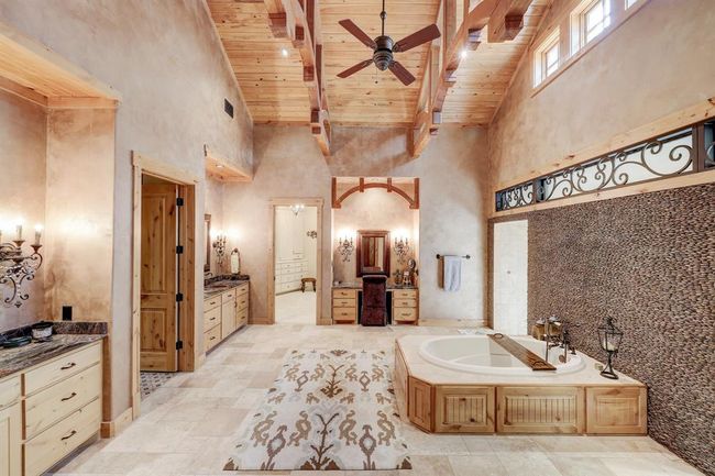 The primary bathroom includes dual sinks, a vanity area, soaking tub, stunning rock wall, and dual shower head walk in shower. | Image 21