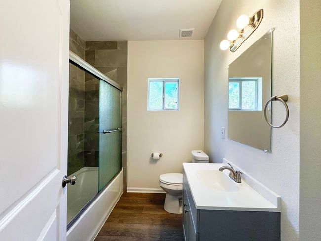 Bathroom with wood finished floors, vanity, toilet, shower / bath combination with glass door, and baseboards | Image 11