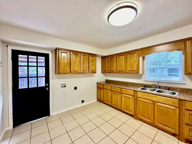 Kitchen with brown cabinets, a textured ceiling, light tile patterned floors, and dark countertops | Image 5