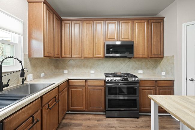Kitchen with stainless steel appliances, a sink, light countertops, dark wood-style floors, and brown cabinetry | Image 12