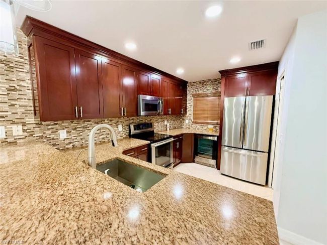 Kitchen featuring light stone counters, a sink, appliances with stainless steel finishes, visible vents, and backsplash | Image 15