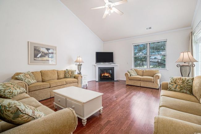 Living area featuring crown molding, healthy amount of natural light, dark wood-style flooring, a ceiling fan, and high vaulted ceiling | Image 5
